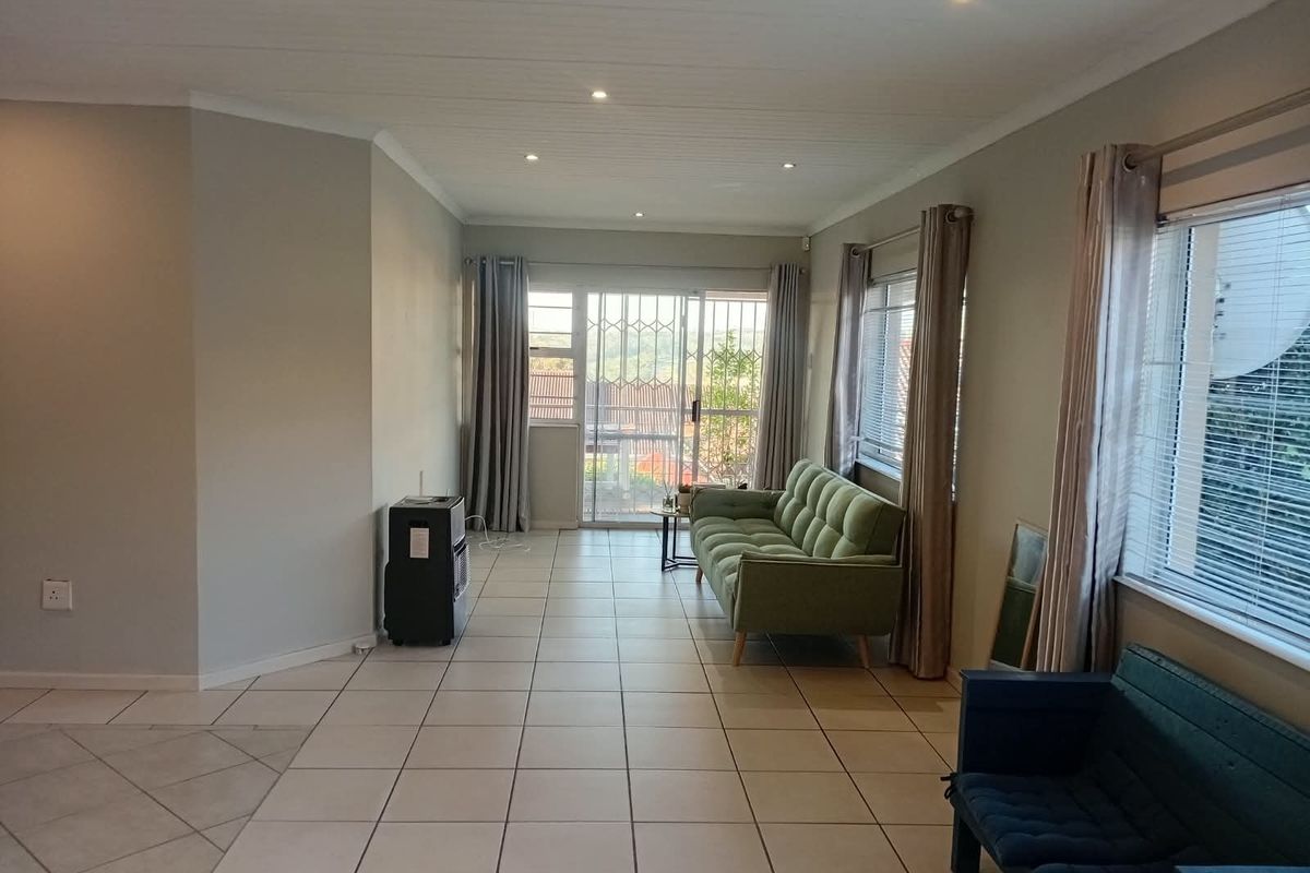 A bright living room featuring neutral tiled flooring, recessed downlighting, and a sliding glass door with security gate leading to an outdoor area.