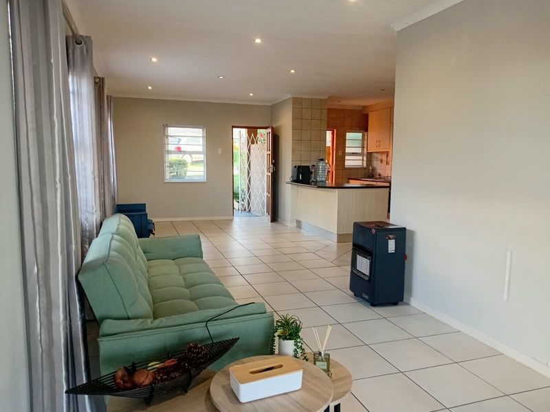 Open-plan living area featuring tiled flooring, recessed lighting, and a breakfast bar connecting to the kitchen, with direct access to the entrance.