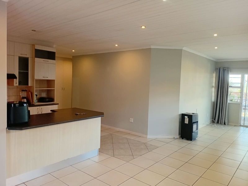 Open-plan living area featuring a kitchen with built-in cabinetry, a breakfast bar, and tiled flooring, leading to a bright living space with sliding doors.