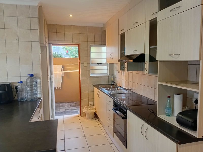 Functional kitchen featuring light-toned cabinetry, dark countertops, integrated electric hob and oven, and tiled finishes with direct access to an outdoor area.