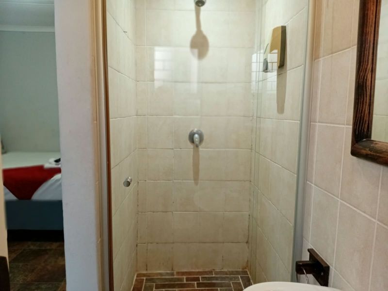 A compact bathroom shower stall featuring tiled walls and flooring, showing signs of wear and requiring maintenance or renovation.