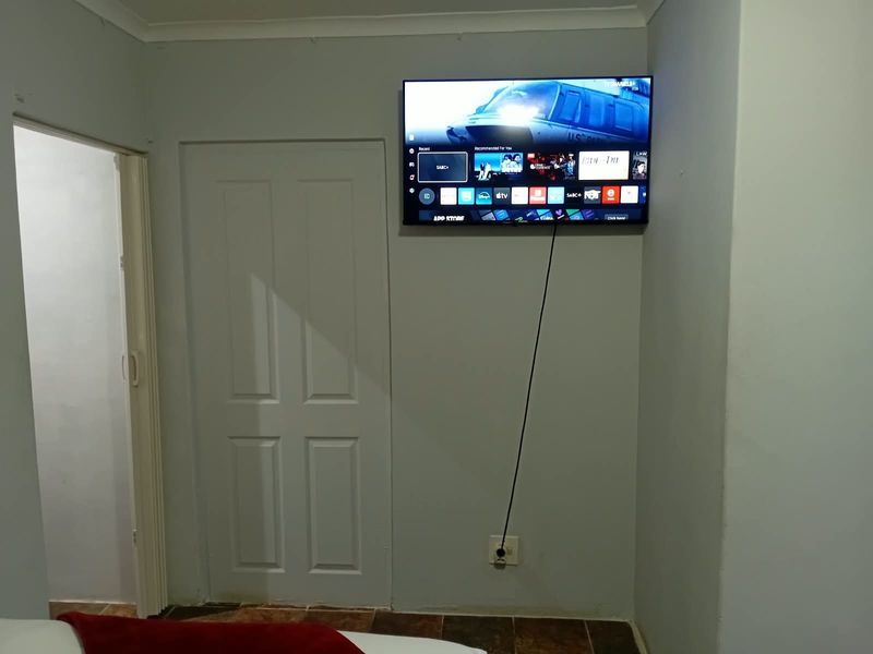 A bedroom interior featuring tiled flooring, a panel door, and a folding door, with a wall-mounted television.