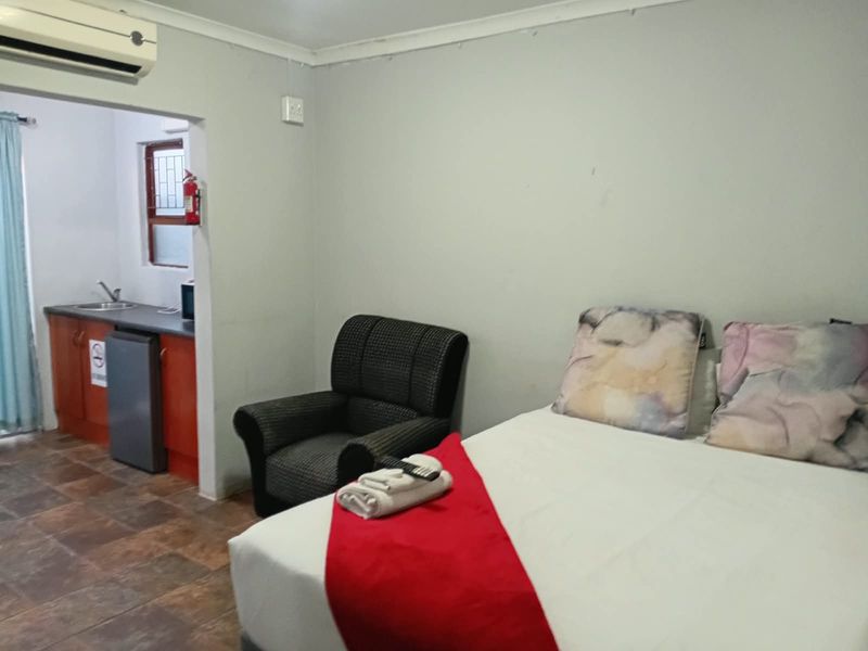 Open-plan studio apartment featuring a bedroom area with an adjoining kitchenette, tiled flooring, and a wall-mounted air conditioning unit.