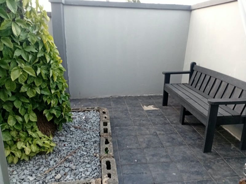 A small outdoor patio area featuring dark tiled flooring, a raised garden bed, and a boundary wall, requiring minor repair to the floor tiles.