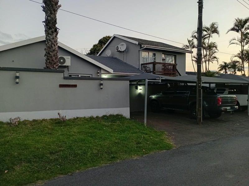 Front exterior view of the apartment building featuring a covered carport, boundary wall, and an upper-level balcony.