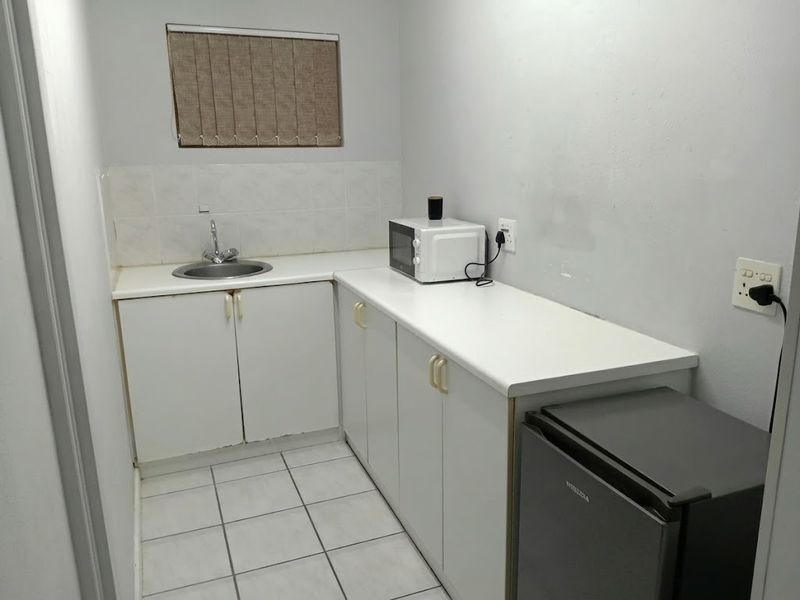 A functional scullery or kitchenette area featuring white built-in cabinetry, a stainless steel sink, tiled splashback, and tiled flooring.