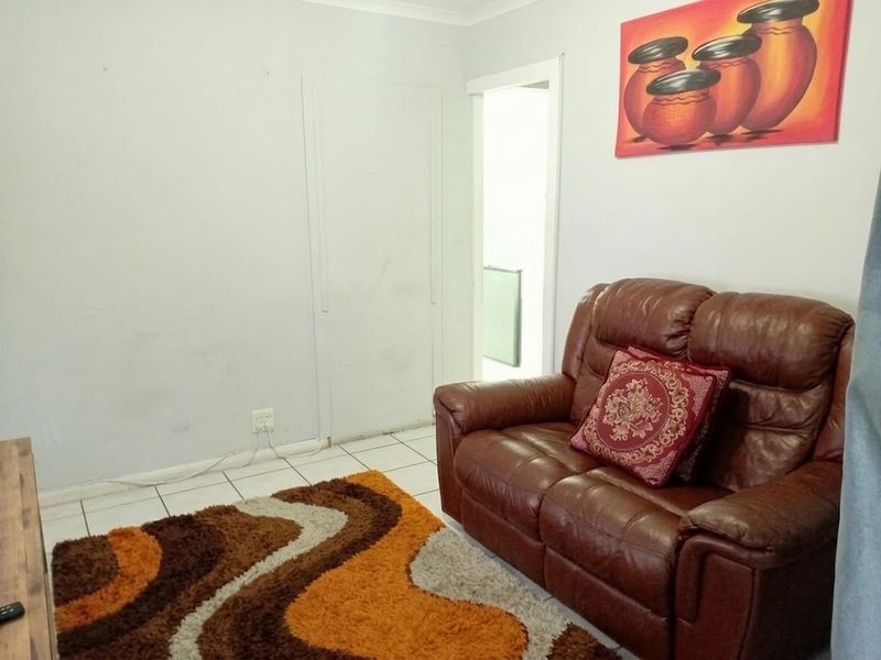 A living room area featuring tiled flooring and plain walls, showing signs of wear and requiring cosmetic updates.