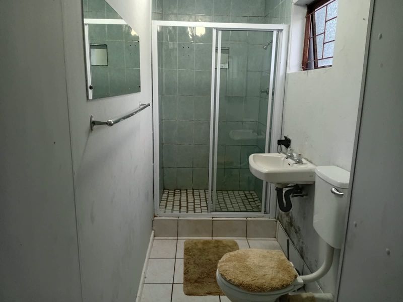 A compact bathroom featuring a shower enclosure, wall-mounted basin, and toilet, requiring cosmetic updates and wall repairs.