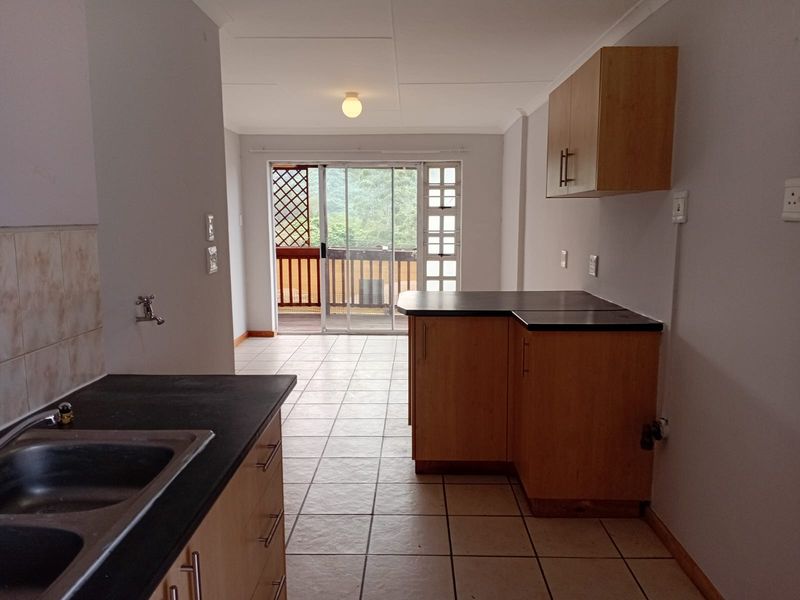 Open plan kitchen area featuring wooden cabinetry, dark countertops, and tiled flooring, leading directly to an outdoor balcony through sliding glass doors.