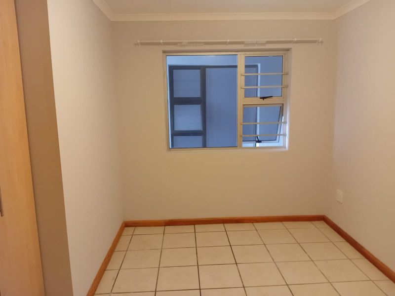 An empty bedroom featuring tiled flooring, wooden skirting boards, and a window fitted with security bars.