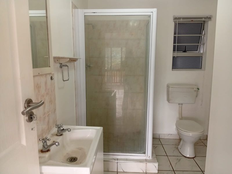 A functional bathroom featuring a shower enclosure, pedestal basin, and toilet, requiring cosmetic updates to finishes and fixtures.