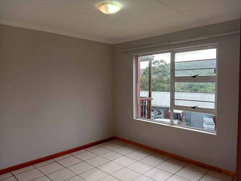 A clean, empty bedroom featuring neutral wall paint, tiled flooring, and a large window with security bars overlooking the surrounding area.