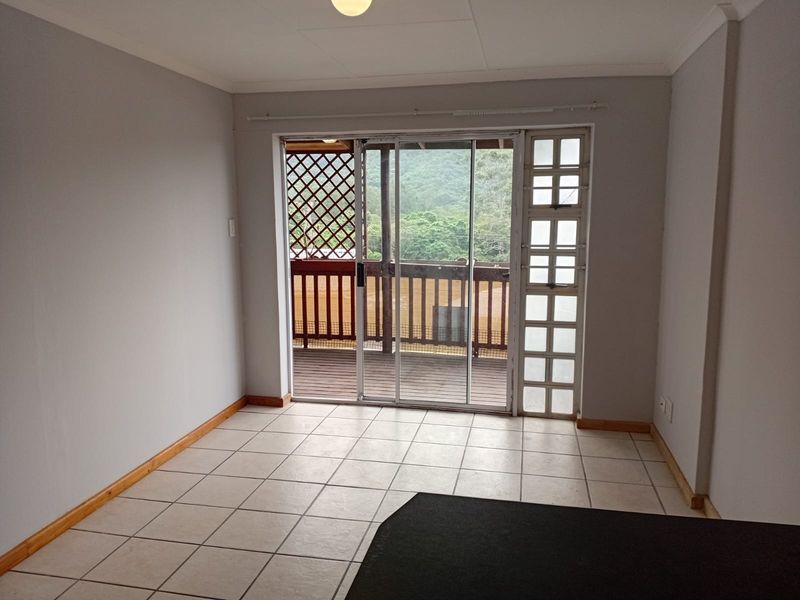 An empty living room featuring tiled flooring and a sliding glass door that opens onto a wooden deck with scenic views.