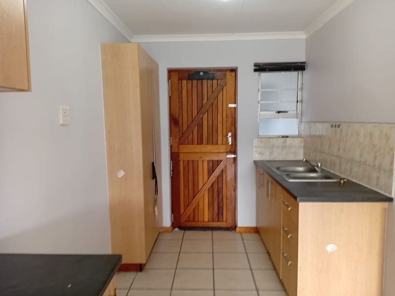 A functional kitchen area featuring built-in cabinetry, a double sink, tiled splashback, and a classic wooden stable door leading outside.
