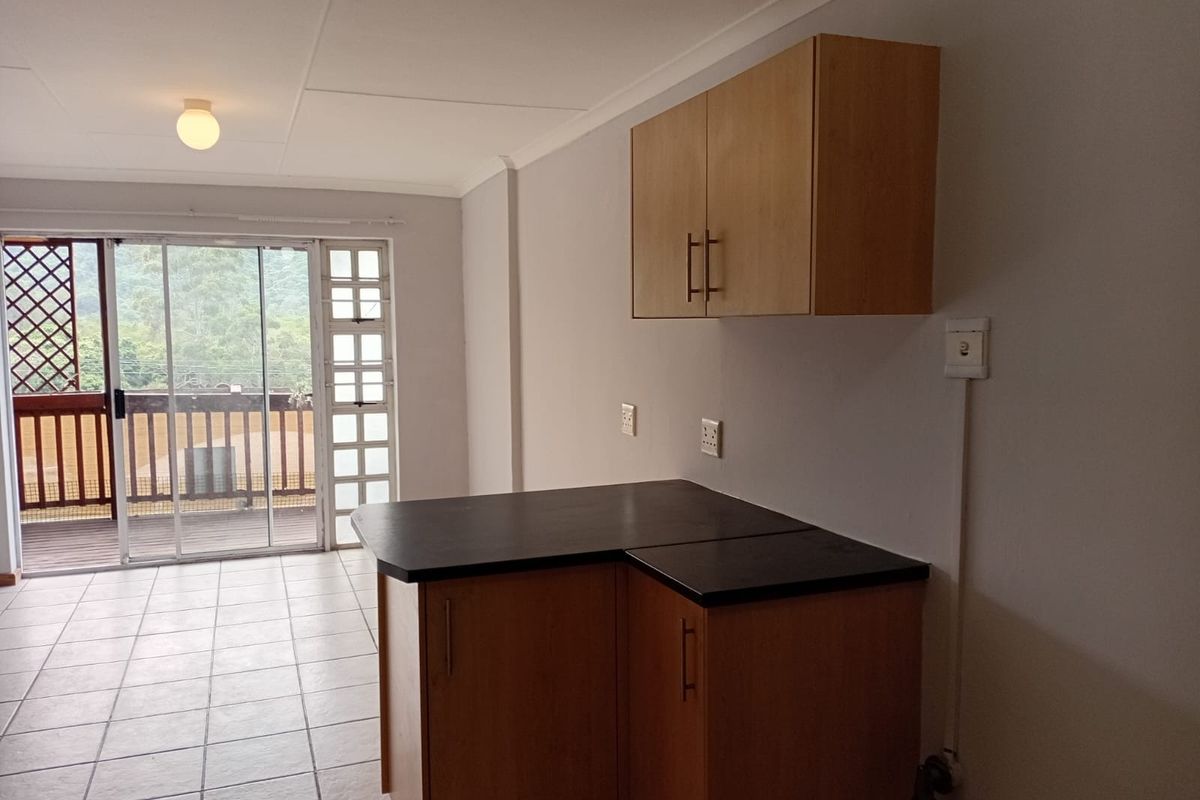 A compact kitchen area featuring built-in cabinetry, dark countertops, and tiled flooring, with direct access to an outdoor balcony through sliding glass doors.