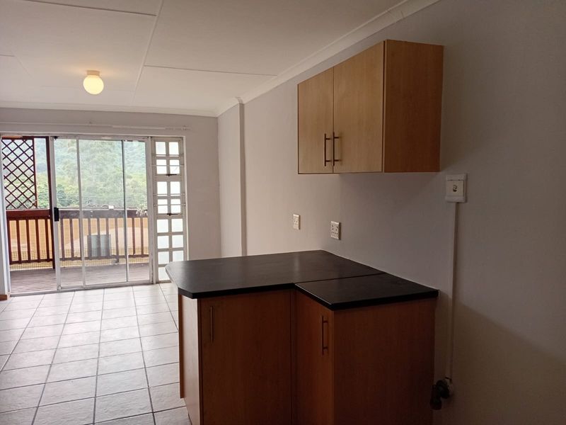 A compact kitchen area featuring built-in cabinetry, dark countertops, and tiled flooring, with direct access to an outdoor balcony through sliding glass doors.