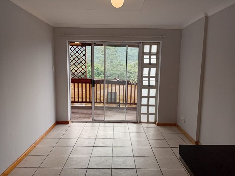 An empty living room featuring tiled flooring and a large sliding glass door providing access to an outdoor balcony area.
