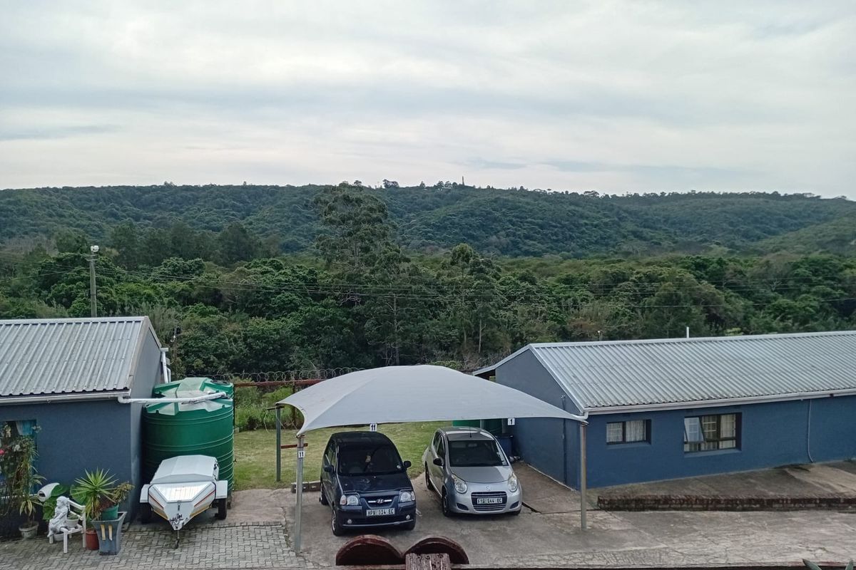 Rear exterior view of the property featuring a paved driveway, shade port parking, and a water storage tank set against a scenic landscape.