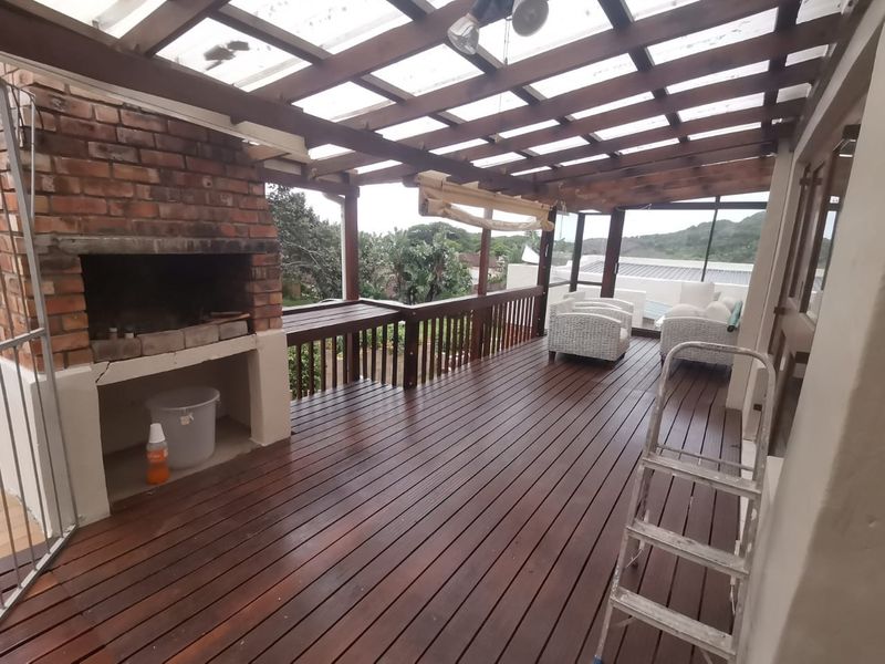 Covered outdoor patio featuring timber decking, a built-in brick braai, and a timber pergola roof, offering a functional space for outdoor entertaining.