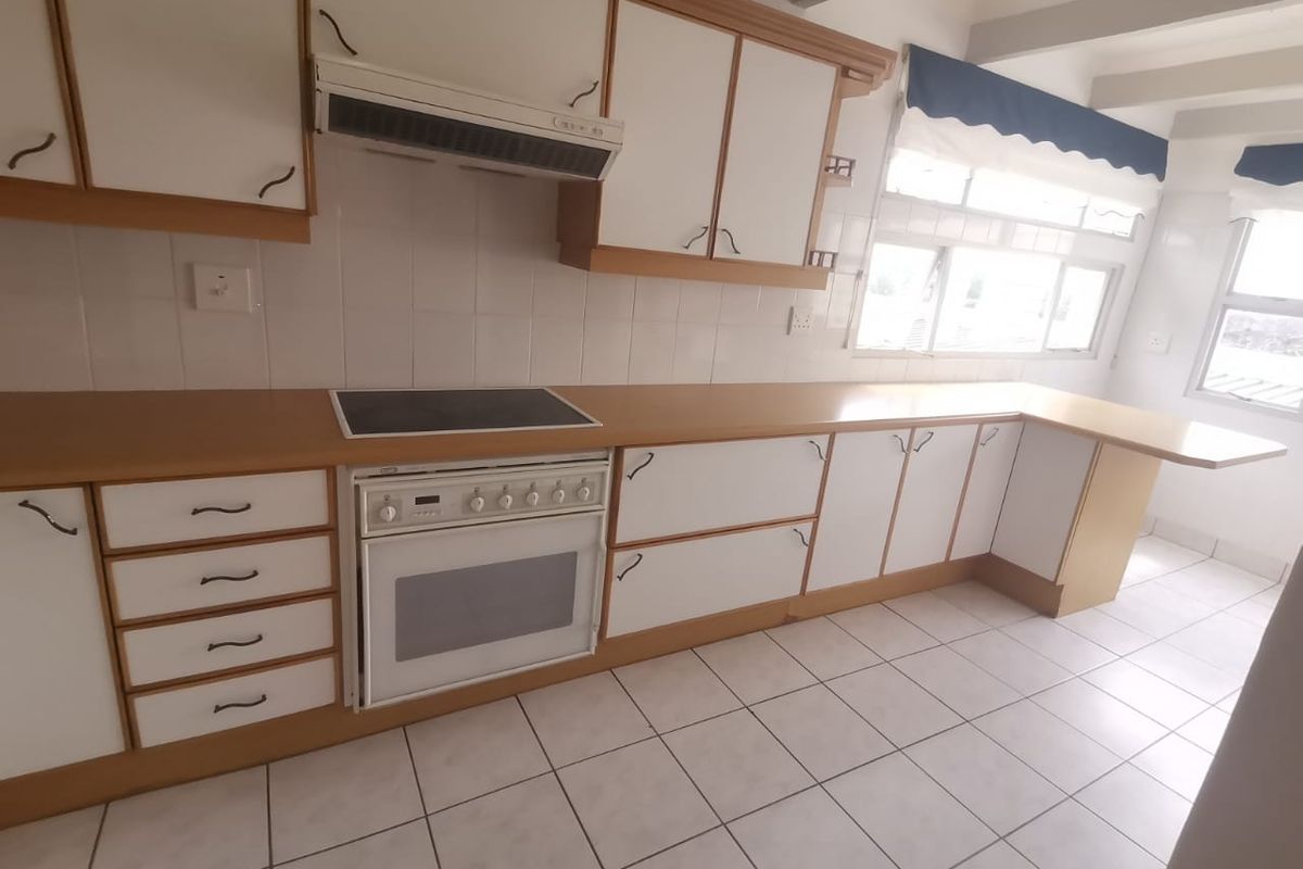A functional kitchen featuring white cabinetry with wood trim, laminate countertops, a built-in electric stove and oven, and tiled flooring.