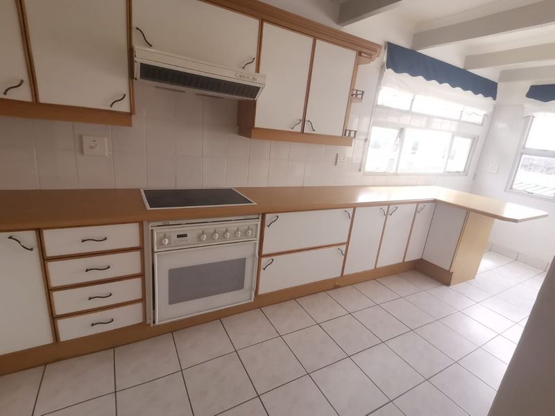 A functional kitchen featuring white cabinetry with wood trim, laminate countertops, a built-in electric stove and oven, and tiled flooring.
