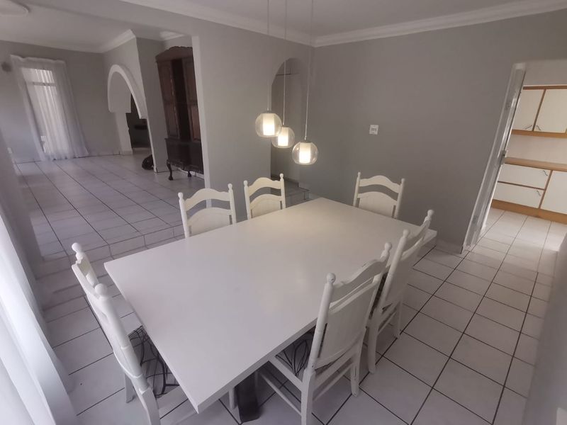 A bright dining room featuring tiled flooring, decorative archways, and modern pendant lighting, with an open-plan layout connecting to adjacent living and kitchen areas.