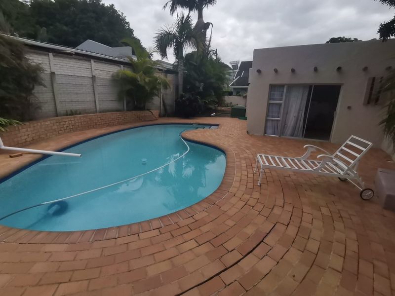 Outdoor pool area featuring a curved swimming pool, brick paving, and a retaining wall, adjacent to a building with sliding door access.