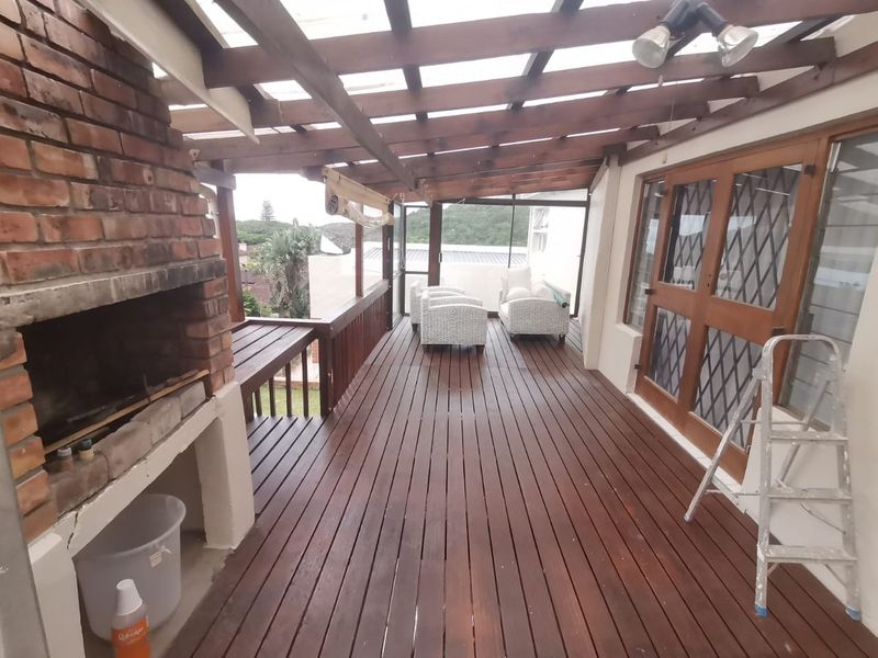 Covered timber deck featuring a built-in brick braai, timber pergola structure, and direct access to the interior through timber-framed glass doors.