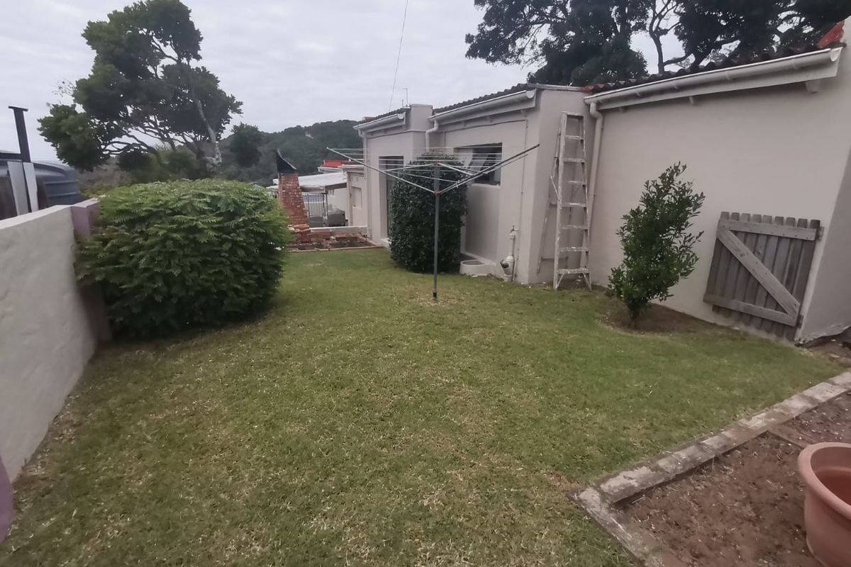 A rear garden area featuring a lawn, a brick chimney structure, and a rotary clothesline, enclosed by masonry boundary walls and a timber gate.