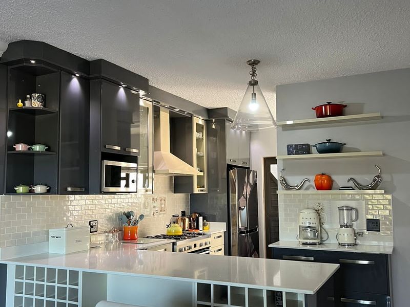 Modern kitchen featuring dark cabinetry, white quartz countertops, subway tile backsplash, and integrated wine storage with stylish pendant lighting.