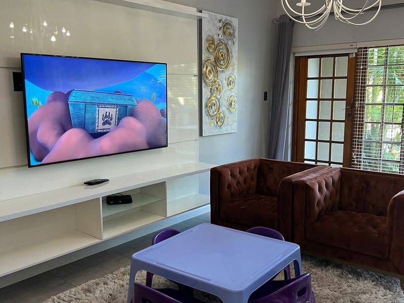 A well-maintained living room featuring a modern built-in media console, elegant chandelier lighting, and direct access to the outdoors through a classic french door.
