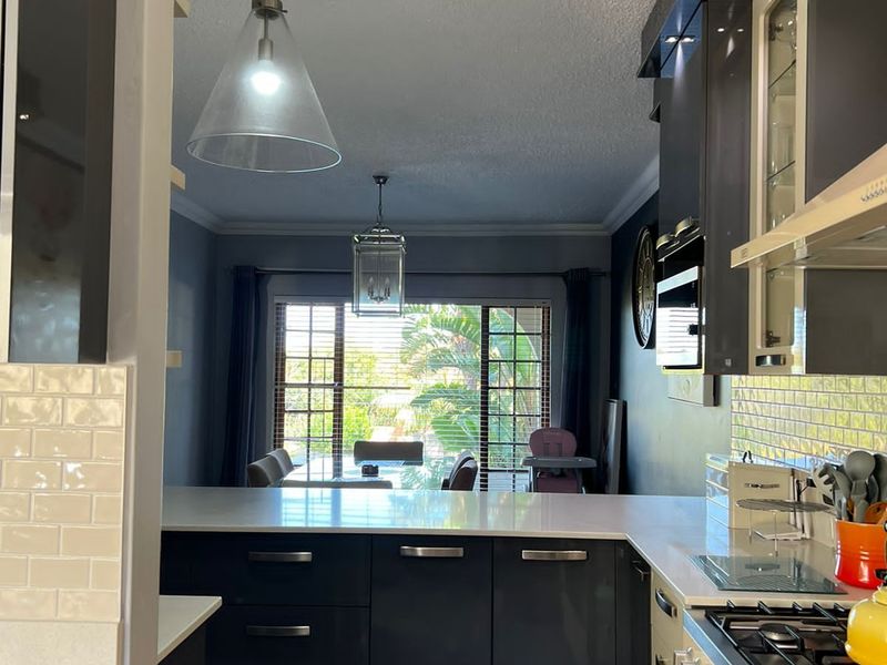 Modern open-plan kitchen featuring high-gloss cabinetry, quartz countertops, subway tile backsplash, and integrated gas cooking appliances, flowing into a bright dining area.