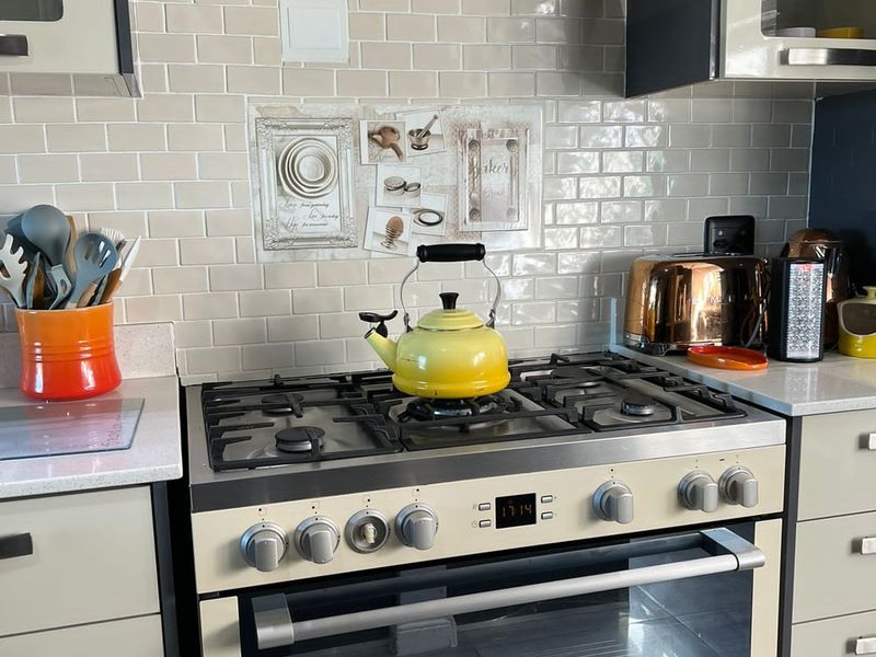 A well-maintained kitchen featuring a cream-colored gas stove with matching extractor fan, subway tile backsplash, and stone countertops.