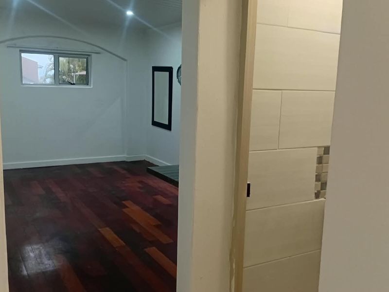 An empty bedroom featuring polished hardwood flooring, recessed ceiling lights, and a view into an adjacent tiled space.