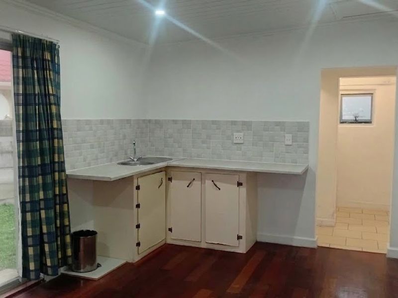 A compact kitchen area featuring timber flooring, basic base cabinetry, a tiled backsplash, and direct access to the garden via a sliding glass door.