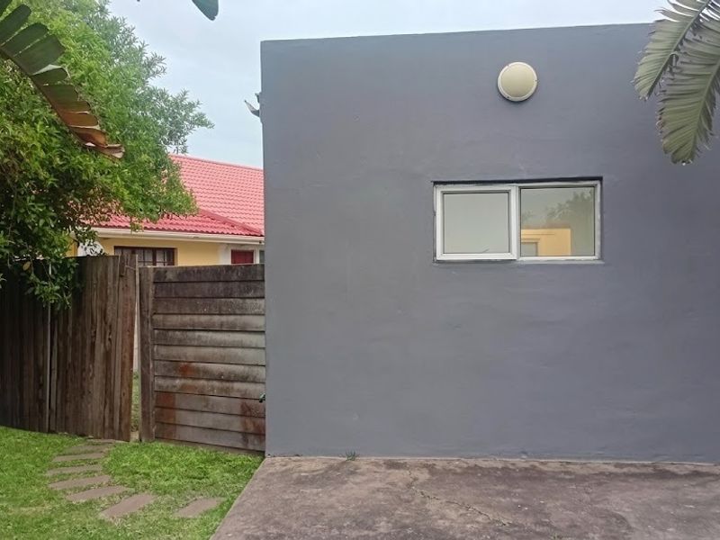 Rear exterior view of the property featuring a grey rendered wall, a sliding window, and a concrete patio area adjacent to a timber fence.