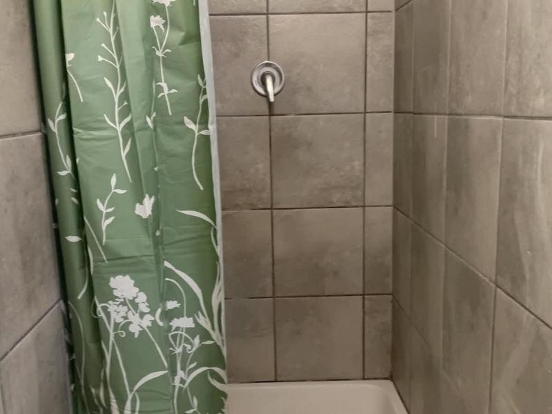 A compact shower enclosure featuring grey wall tiles and a standard shower mixer fixture.