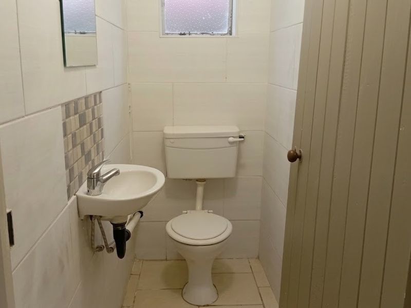 A compact, functional bathroom featuring a wall-mounted basin, standard toilet, and tiled finishes throughout.
