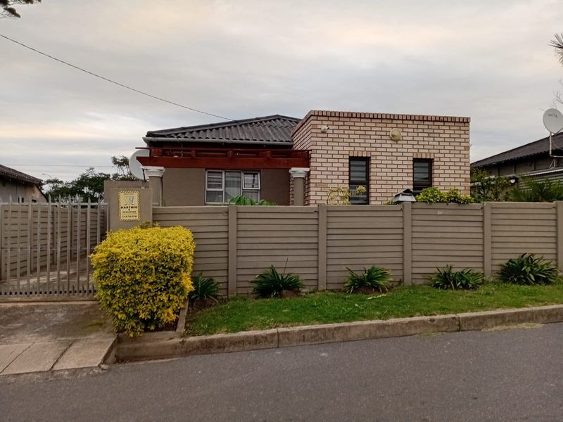 Front view of a single-story house featuring a facebrick facade, tiled roof, timber pergola, and a secure precast concrete boundary wall with a metal gate.