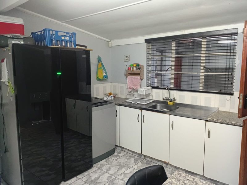A functional kitchen featuring white cabinetry, laminate countertops, a stainless steel sink, and tiled flooring with a window providing natural light.