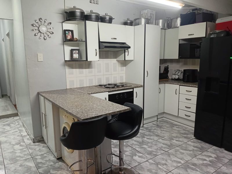 A functional kitchen featuring white cabinetry, laminate countertops, an integrated electric hob and oven, and tiled flooring with a breakfast bar area.