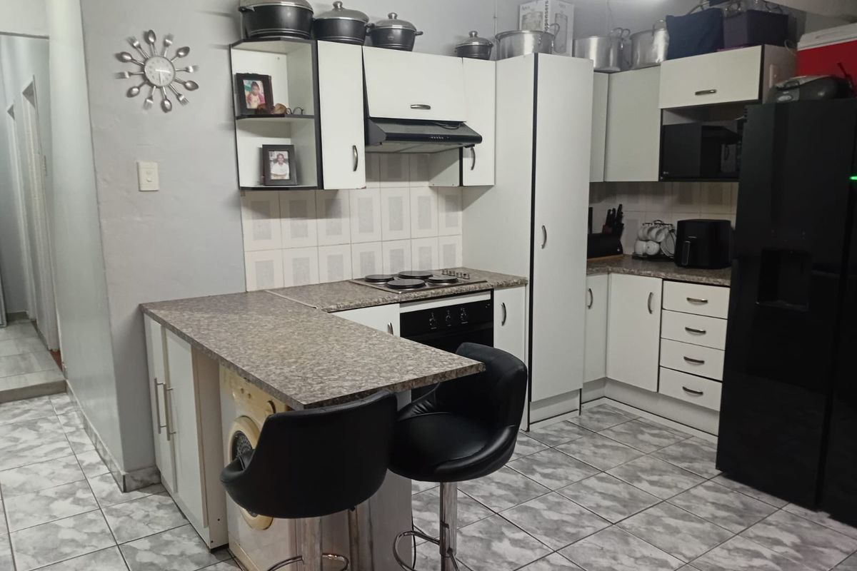 A functional kitchen featuring white cabinetry, laminate countertops, an integrated electric hob and oven, and tiled flooring with a breakfast bar area.