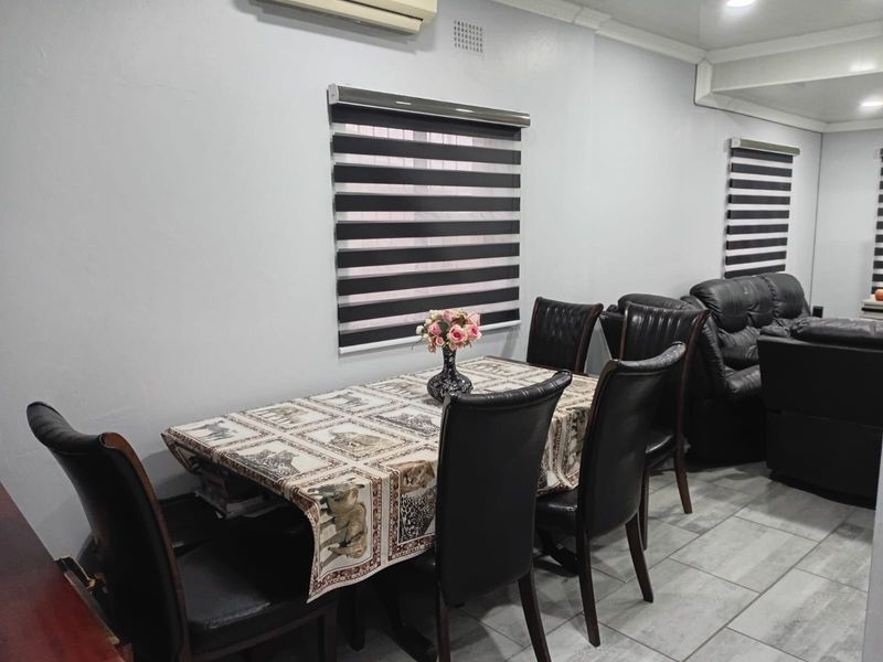 Dining area featuring tiled flooring, modern roller blinds, and a wall-mounted air conditioning unit, providing a functional and well-lit space.