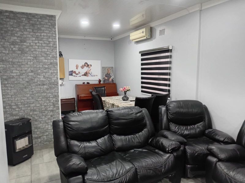 A living room featuring a faux brick accent wall, tiled flooring, recessed lighting, and a wall-mounted split-system air conditioning unit.