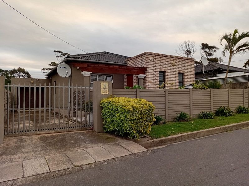 Front view of a single-story house featuring a brick and rendered facade, tiled roof, perimeter wall, and a secure metal driveway gate.