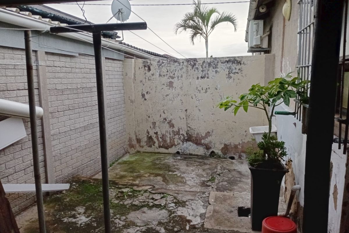 A rear exterior courtyard area featuring a concrete surface and boundary wall, currently showing significant signs of wear and weathering.