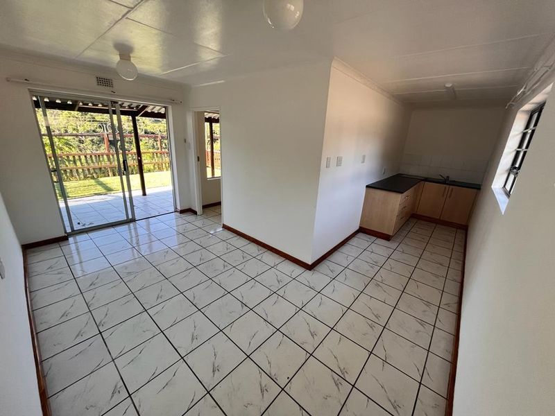 Open plan living area featuring tiled floors, a compact kitchen with built-in cabinetry, and sliding glass doors leading to an outdoor patio area.