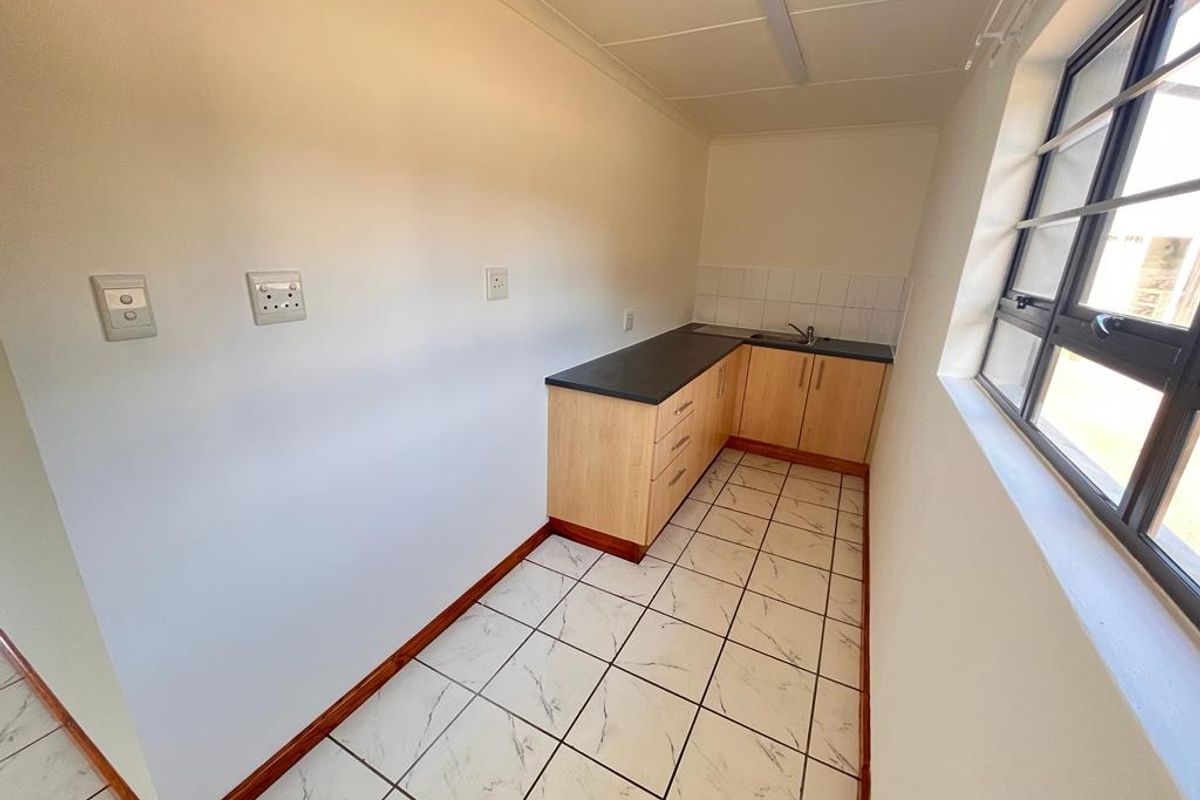 A compact, functional scullery area featuring built-in cabinetry, a stainless steel sink, and tiled flooring, providing additional prep and wash-up space.