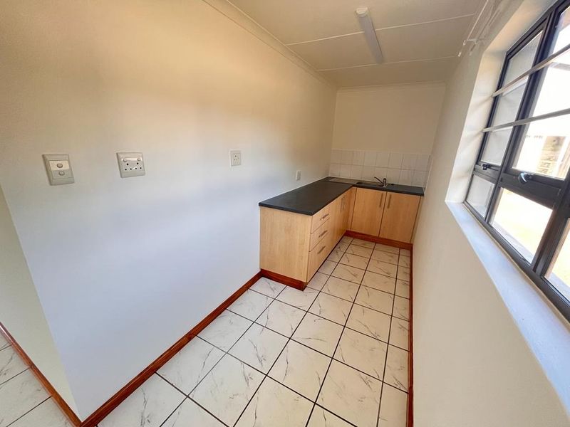 A compact, functional scullery area featuring built-in cabinetry, a stainless steel sink, and tiled flooring, providing additional prep and wash-up space.