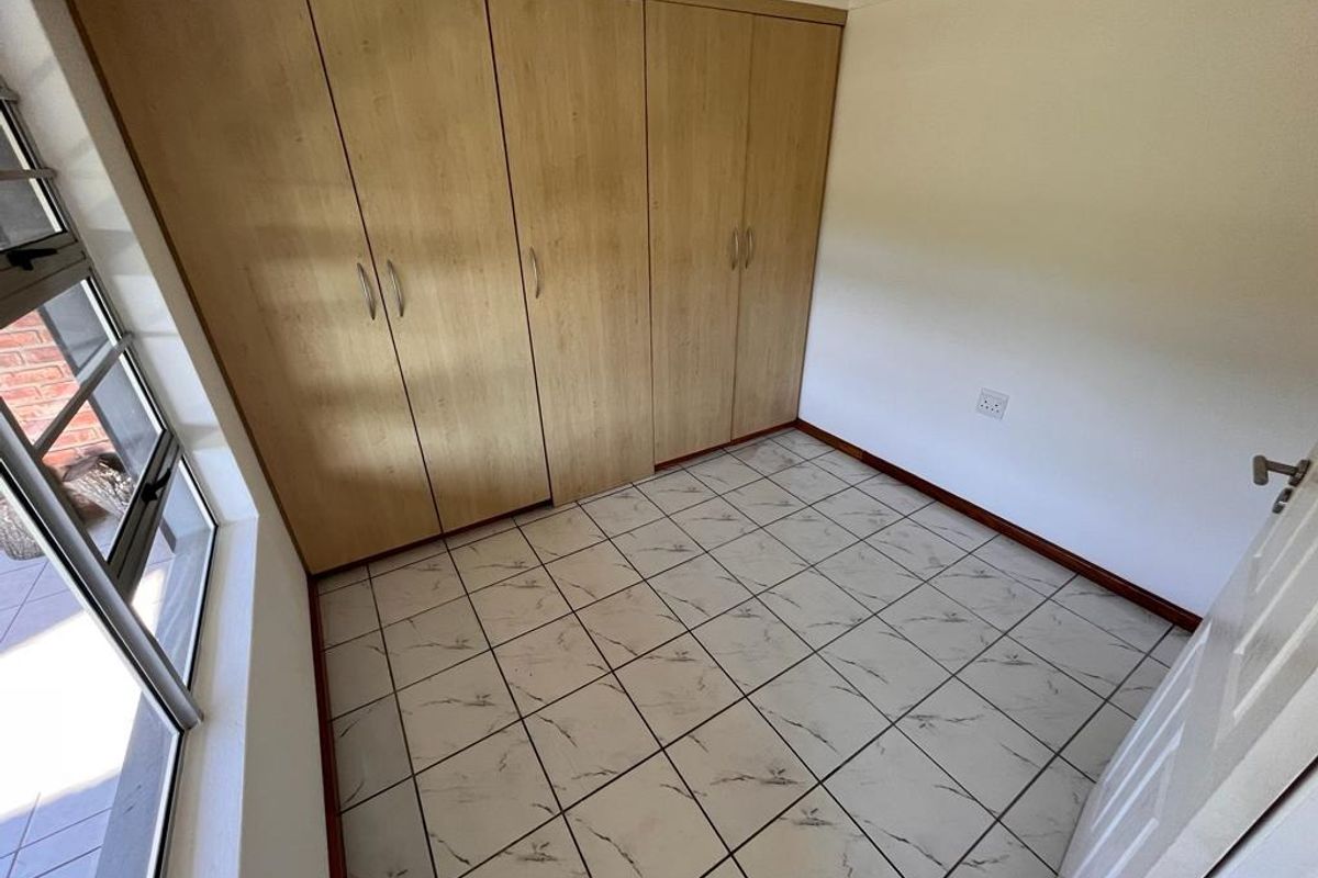 A bright, empty bedroom featuring tiled flooring and ample built-in cupboard storage, offering a clean and neutral space ready for personalization.